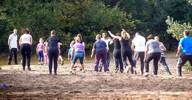 Een groep mensen zijn actief aan het springen tijdens een bootcamp les in een bos