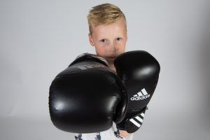 Een jonge jongen met bokshandschoenen aan die een vuist uitsteekt naar de camera