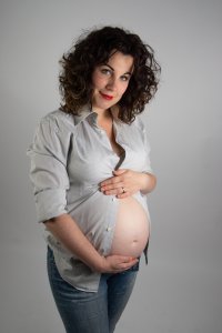 Een zwangere vrouw die haar buik bloot heeft door knoopjes van een blouse niet volledig te sluiten. Op de afbeelding staat ze met haar handen over haar buik om de nadruk op de baby te leggen. 