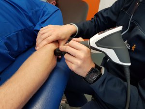 Een fysiotherapeute die een shockwave therapie apparaat gebruikt op een blote arm van een patiënt
